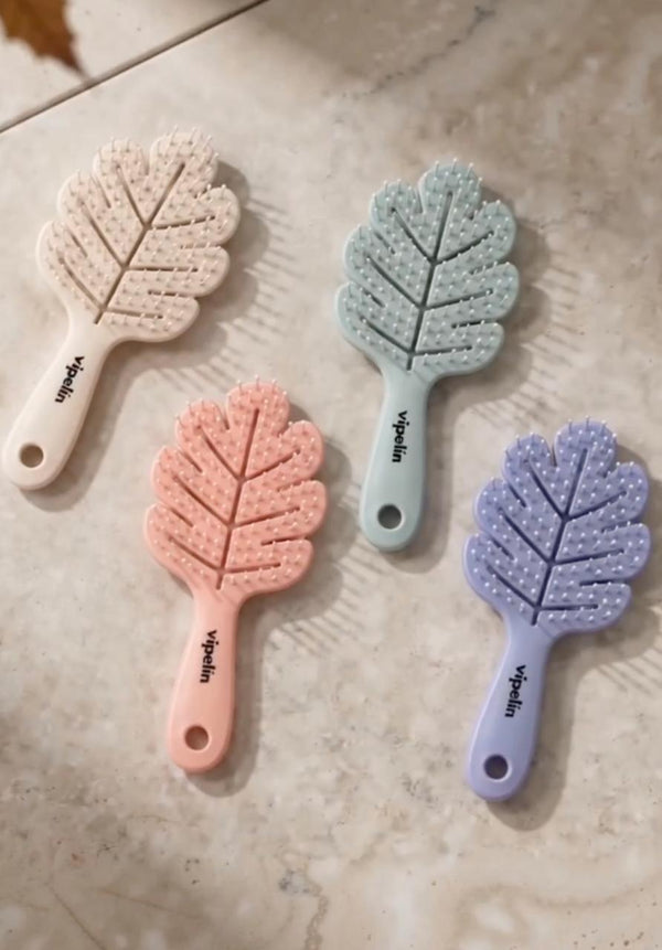 Colección de cepillos desenredantes en forma de hoja de vipelín en tonos pastel (beige, menta, rosa y lila) dispuestos sobre una superficie de mármol. Accesorios ergonómicos y flexibles diseñados para desenredar el cabello suavemente sin tirones, reducir la rotura capilar y masajear delicadamente el cuero cabelludo.