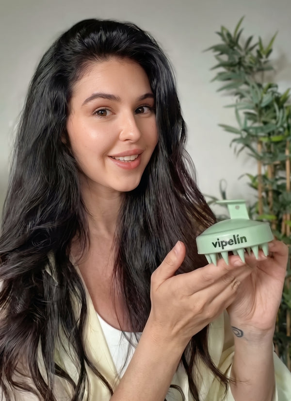 Mujer joven mostrando el masajeador capilar de silicona de vipelín en un ambiente luminoso. Accesorio diseñado para estimular la microcirculación del cuero cabelludo, facilitar la aplicación de tratamientos y promover la salud y el crecimiento del cabello desde la raíz.