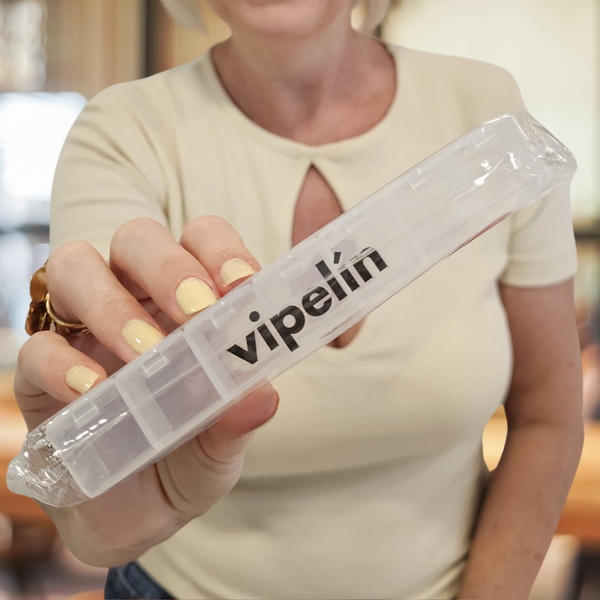 Mujer sosteniendo el pastillero semanal organizador de vipelín para cápsulas y tratamientos capilares. Accesorio práctico y transparente diseñado para planificar las tomas diarias, facilitar la constancia en el tratamiento y mantener una rutina capilar organizada tanto en casa como de viaje.